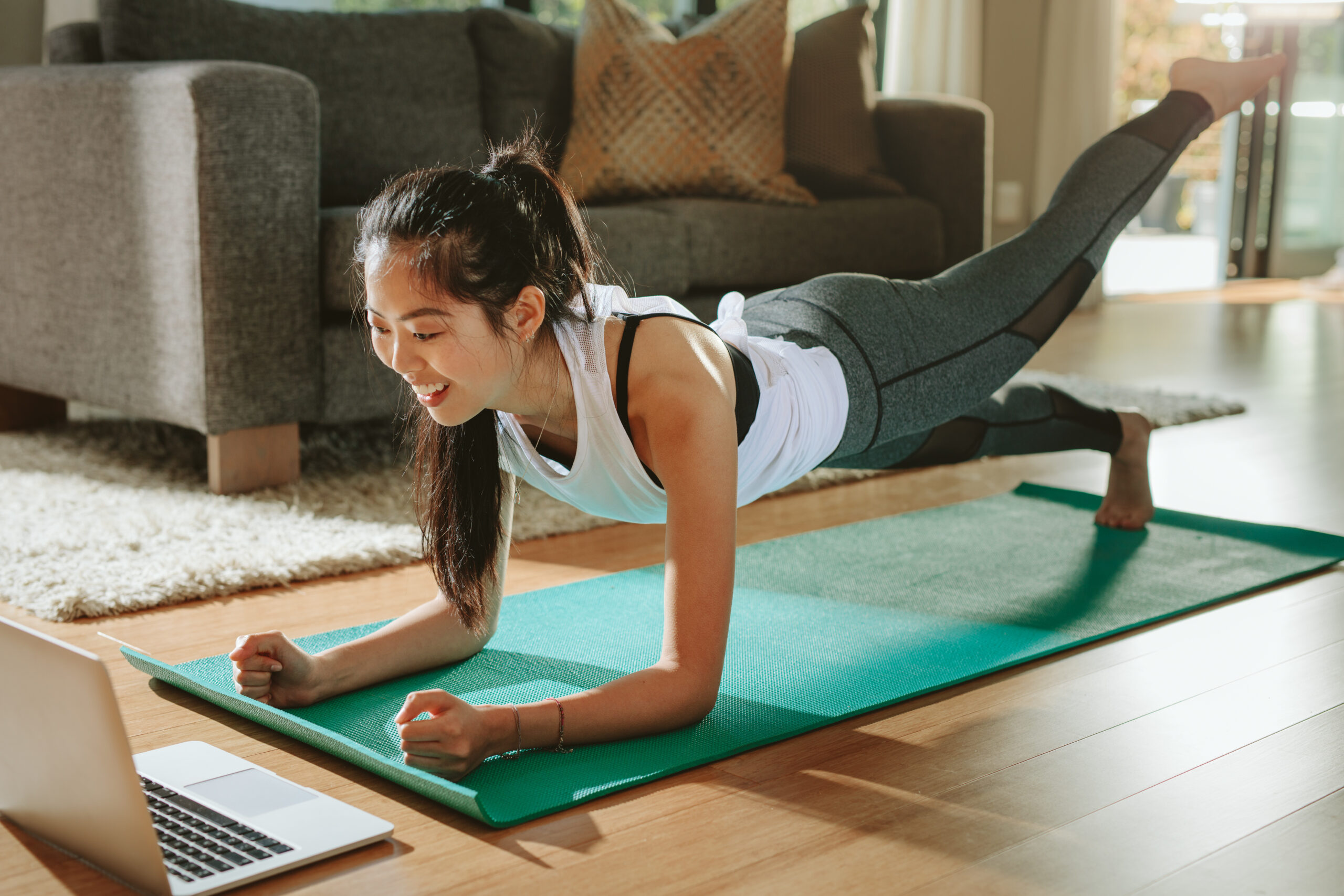 Mujer en su sala de estar haciendo ejercicio en línea en su computadora portátil y usando el ejercicio como una intervención en el estilo de vida para combatir el dolor crónico de su endometriosis.