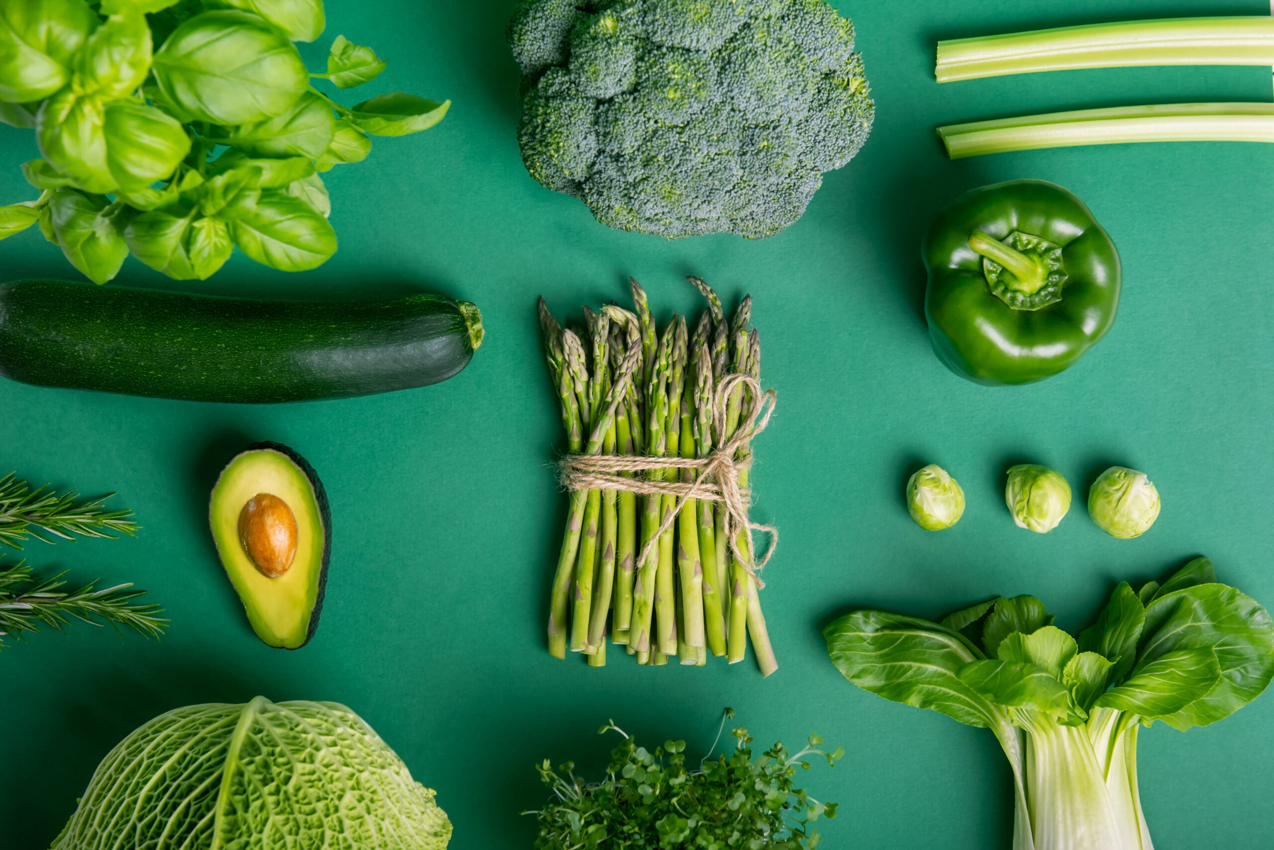 Flat lay of green vegetables on a green background, all a part of a healthy diet that can help reduce POPs and metabolic syndrome.