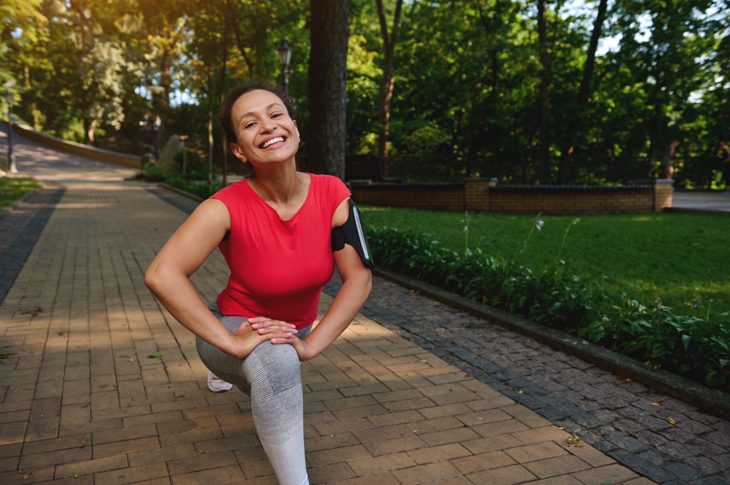 Smiling Black woman doing lunges in the park to help her microbiome and immune disease.