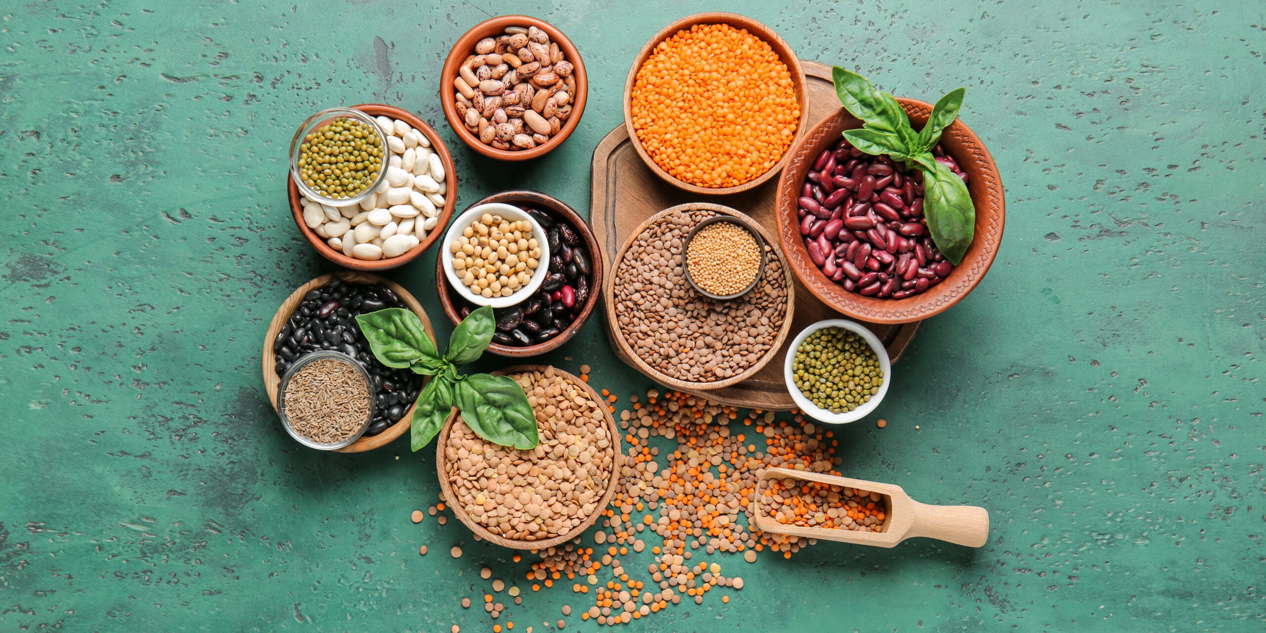 Flat lay of raw beans and spices on green background symbolizing a nutrient dense diet can help defer toxicant exposure and reduce colorectal cancer.