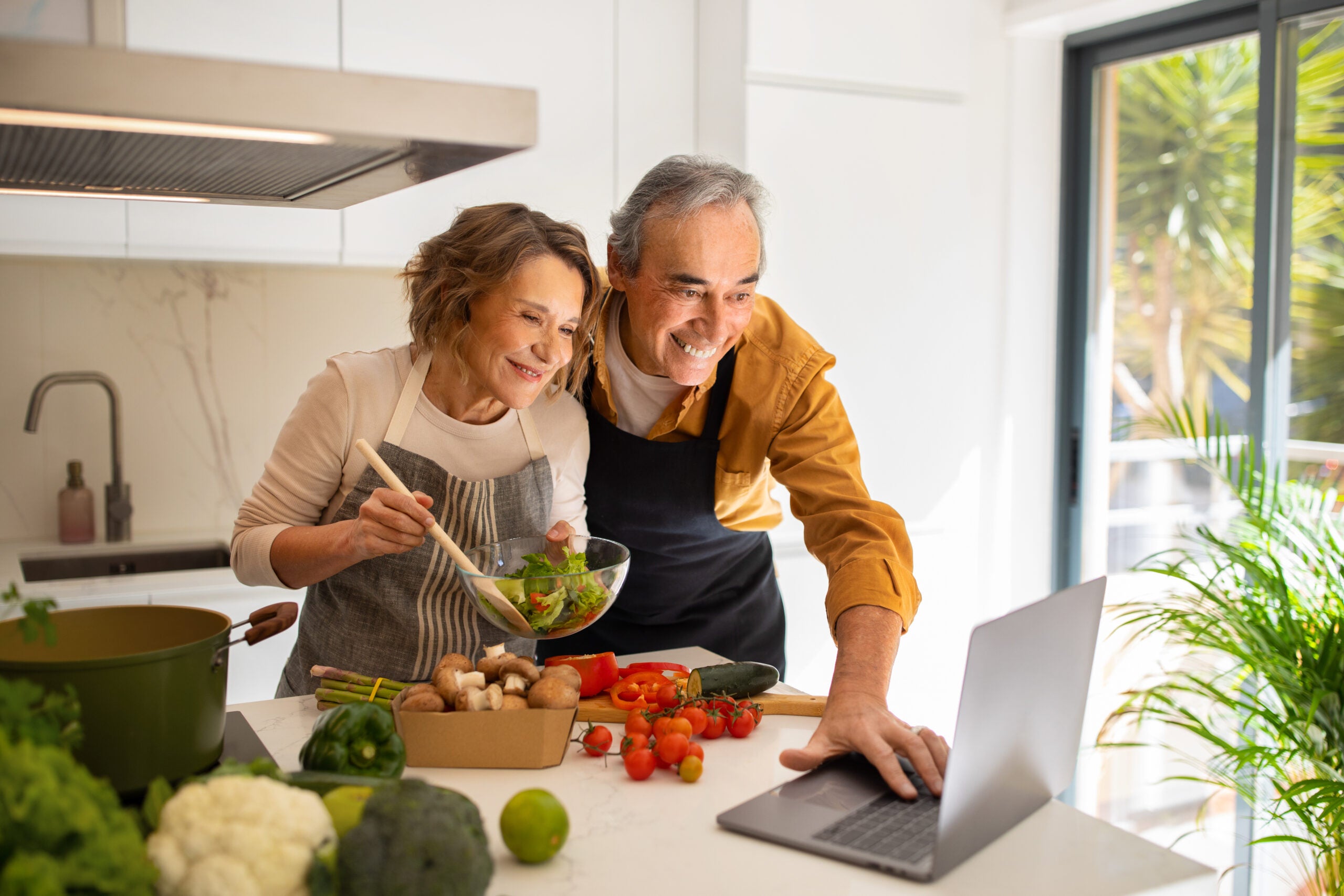 Iddle aged couple smiling and cooking in kitchen together feeling empowered by the nutrition interventions her functional medicine doctor gave her.