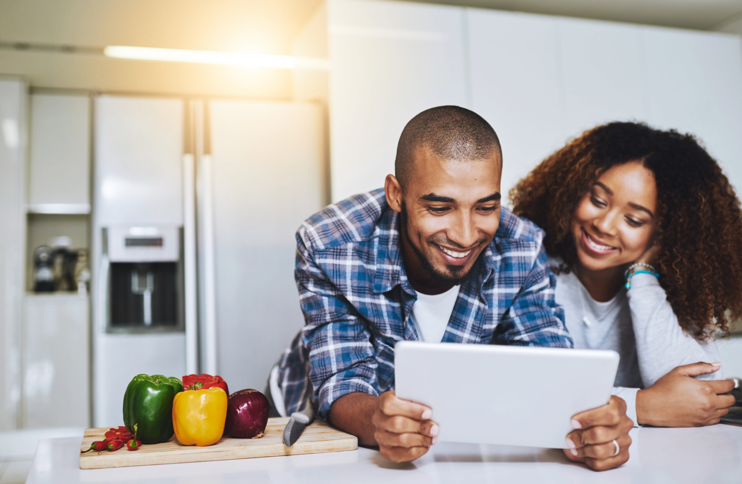 A couple smiling and reading a recipe in their kitchen next to vegetables, happy to be using nutrigenomics as a functional medicine treatment for their health.