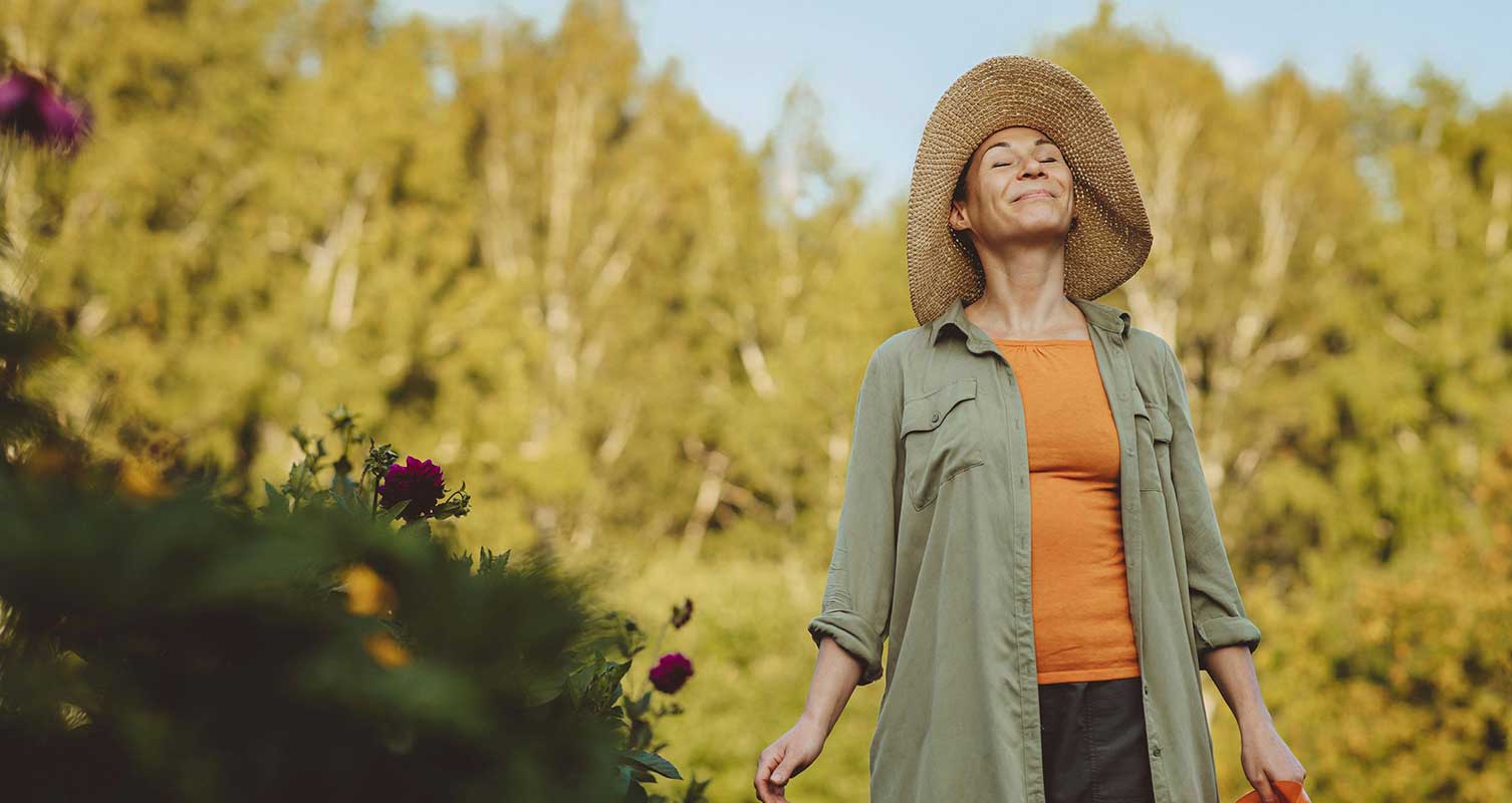 Women in a large hat facing towards the sun and smiling as she grounds in nature and uses lifestyle therapies to reduce her GERD symptoms.