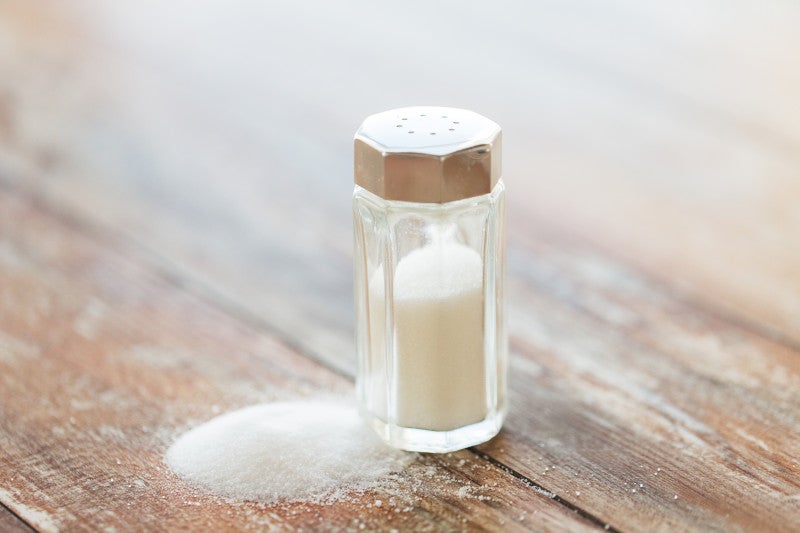 Table salt on a wooden table. Research links increased sodium intake with hypertension risk and Type 2 Diabetes.