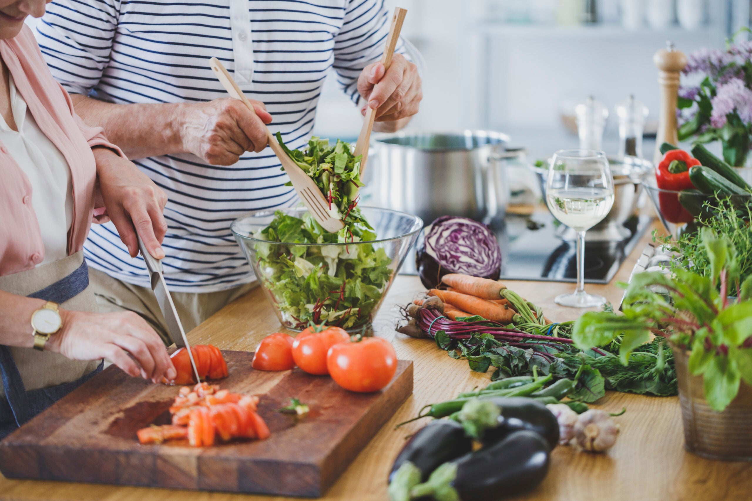 Close-up of elderly couple cutting tomatoes and tossing salad while preparing healthy dinner, which is a great functional medicine solution for chronic pain.