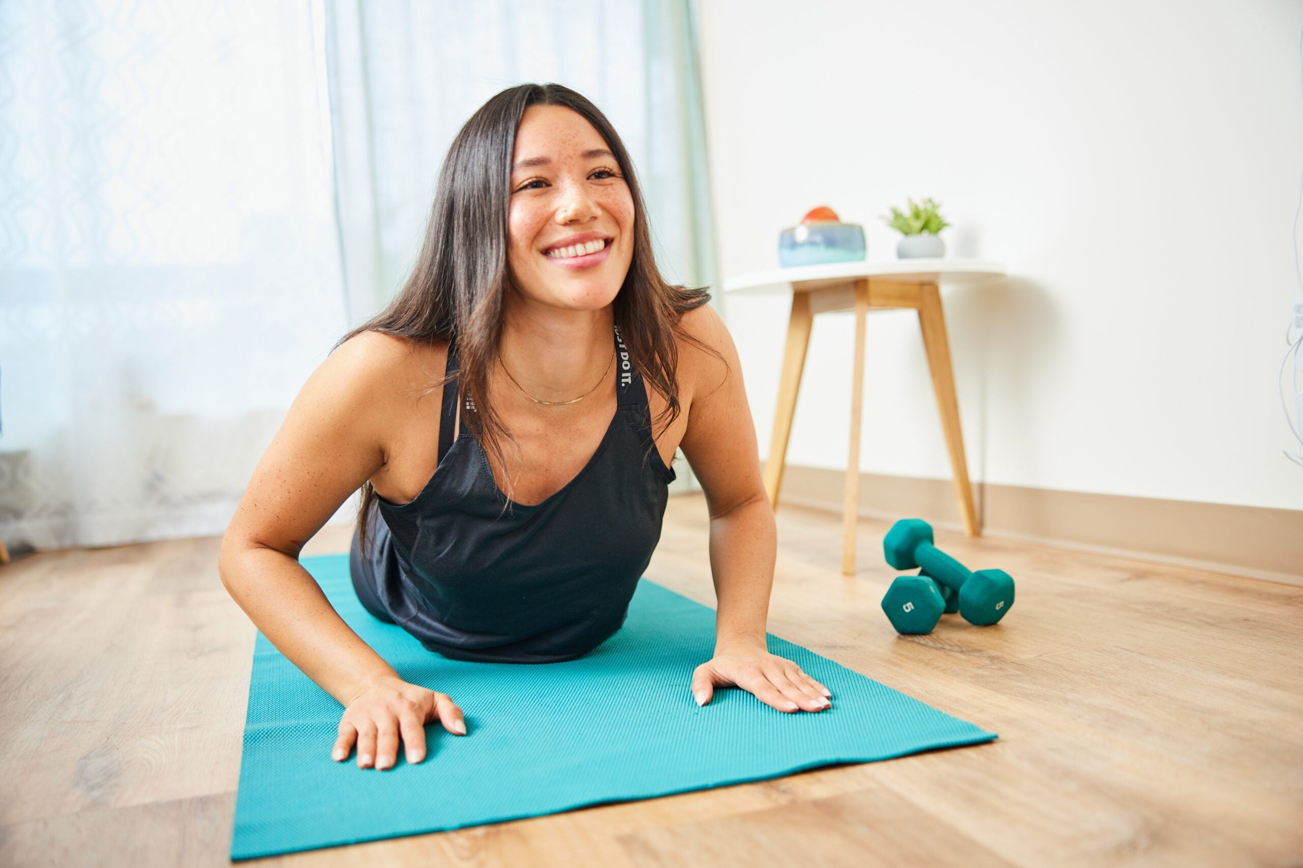 Joven mujer sonriendo en una postura de yoga, utilizando el yoga como una manera de reducir los síntomas de SOP.