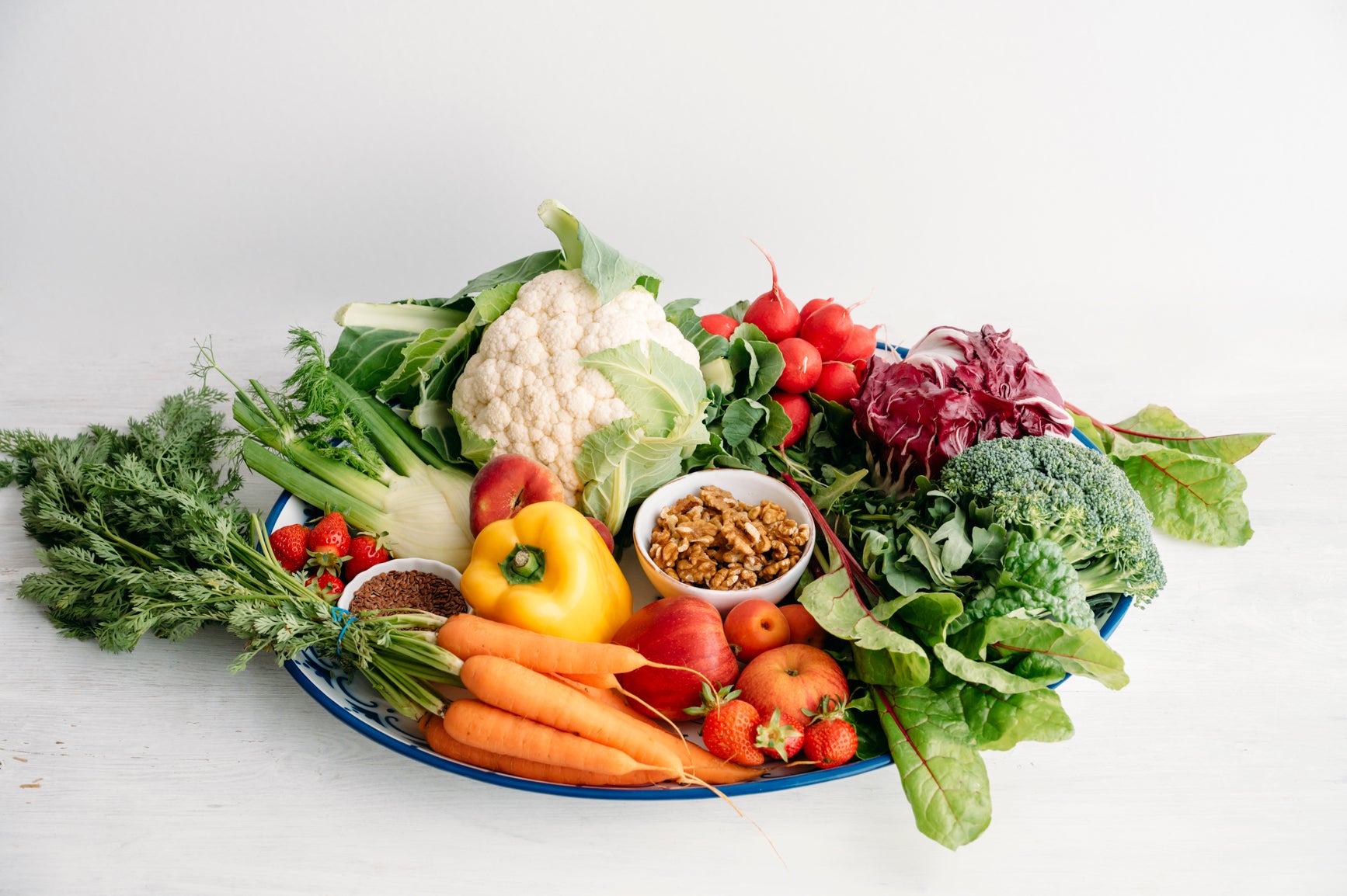 Una bandeja azul de frutos secos y vegetales frescos y coloridos que respaldan la salud intestinal y de las mitocondrias, sobre un fondo blanco.